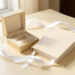 Coffret de baptême élégant accompagné d’un bijou, d’un livre souvenir vierge et d’un ruban blanc sur une table lumineuse.