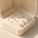 Écrin élégant ouvert contenant plusieurs bijoux délicats et symboliques pour enfant, disposés sur un velours ivoire dans une ambiance douce et lumineuse.